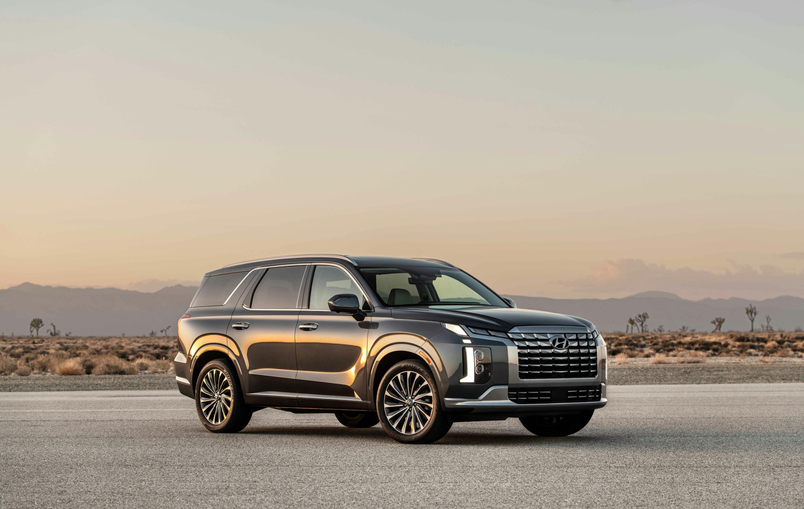 A sleek SUV parked on an empty road against a serene desert backdrop during sunset.